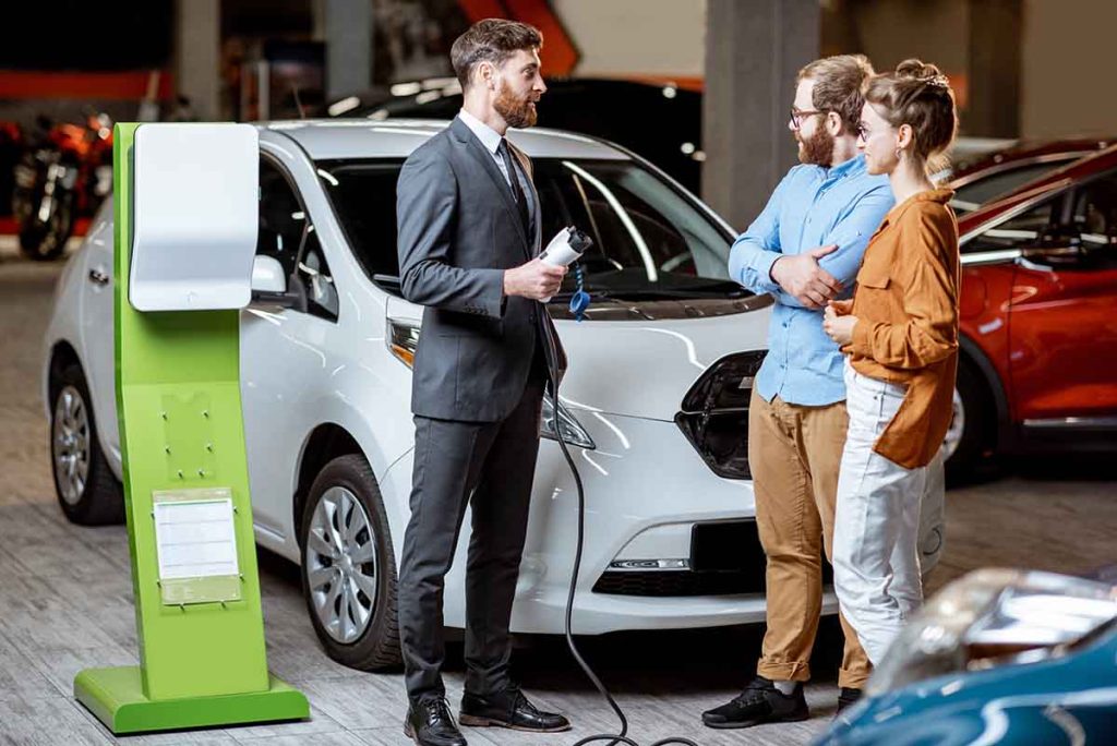 Sales manager showing car charging station to a young couple
