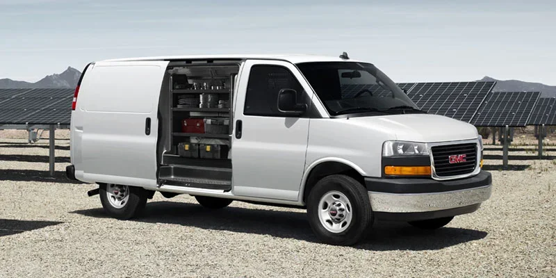 White GMC Savana cargo van with open side door at a solar farm.
